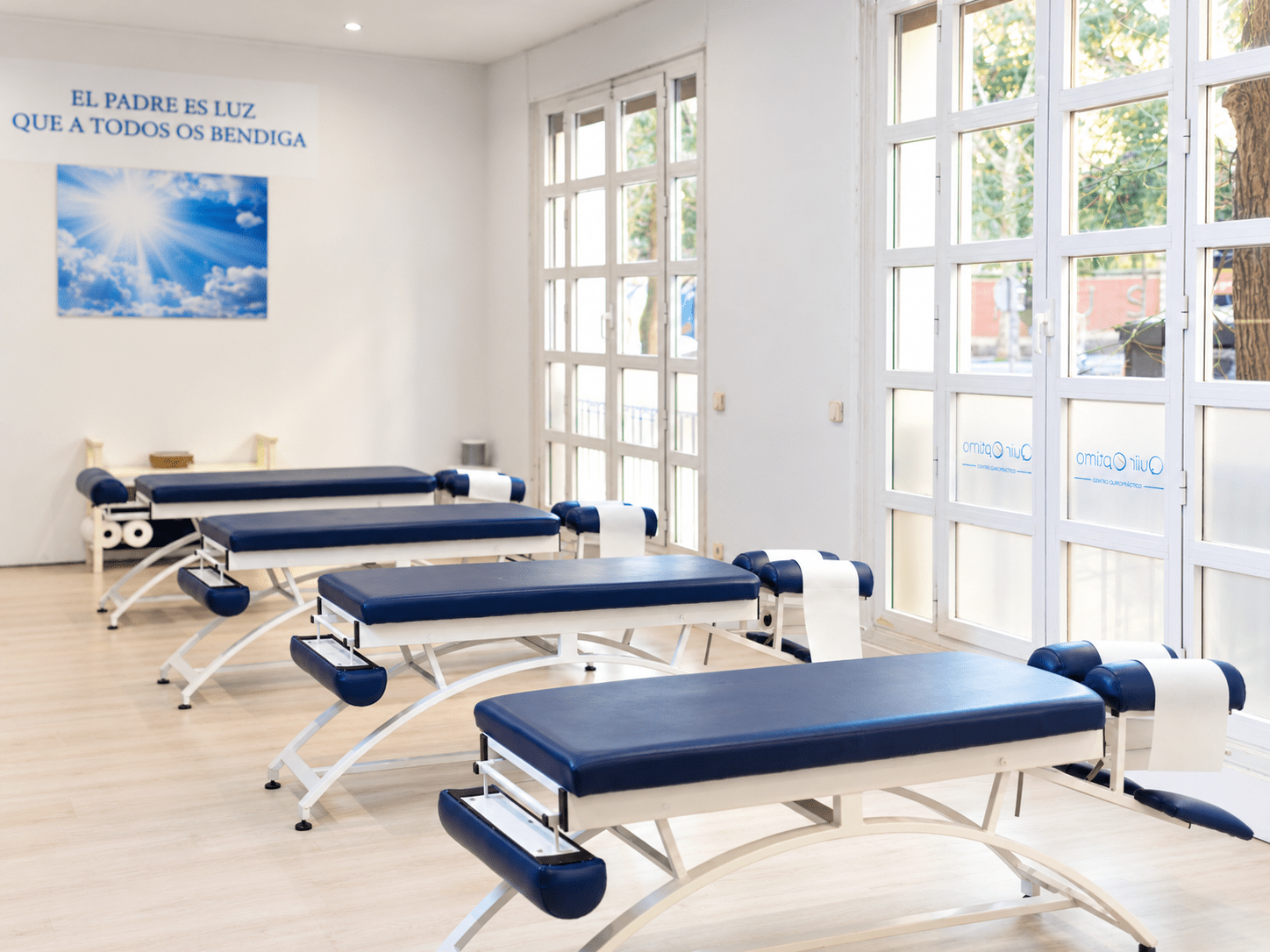 Sala de Network Spinal de Quiroptimo en Madrid, con camillas azules y grandes ventanas.
